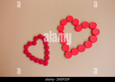 Environmentally friendly Valentine's Day gift. Two hearts formed out of plastic bottle caps on brown paper background. Stock Photo