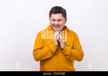 Cunning middle aged man clasping hands and planning evil tricky prank or scheming, cheating with sly smile, wearing urban style hoodie. Indoor studio shot isolated on white background. Stock Photo
