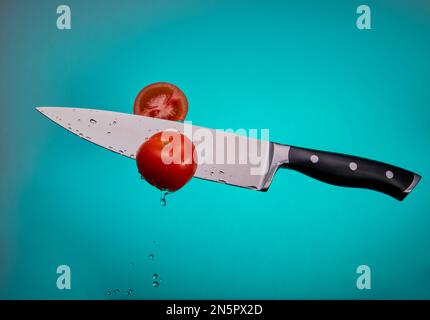 Flying chef's knife cutting threw tomatoes isolated on a blue gradient background. Stock Photo