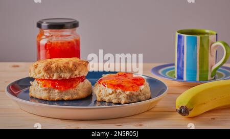 Fresh scones with butter and jam on them with a cup of coffee and a banana. Stock Photo