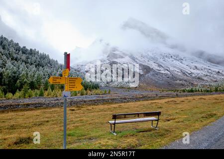 A bench to rest and distinctive yellow direction signs.  Gemmi Pass Trail. Switzerland's Bernese Oberland Stock Photo