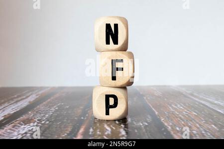 three wooden cubes with letters - nfp on yellow table, space for text in right. front view concepts, flower in the background. nfp - short for Non-Far Stock Photo