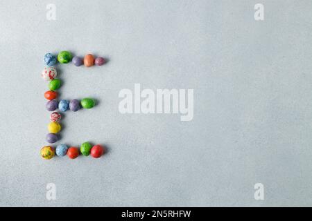 Candy chocolate eggs shaped in letter E, name, Happy Easter concept. Light gray, concrete background. Preparation for holiday.  Copy space Stock Photo