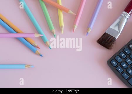 Pastel colored pencils with a brush and a calculator, top view on pink background, back to school concept, copy space Stock Photo