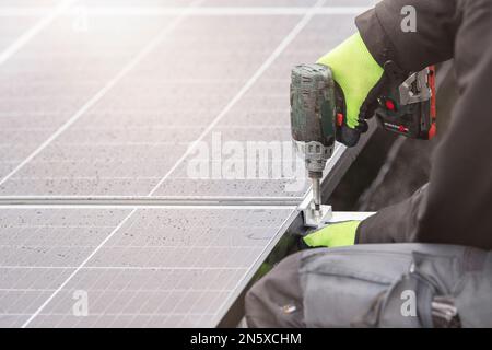 The solar panel installer twists the modules together using aluminum fasteners and a cordless drill. Rooftop installation work and security, concept Stock Photo