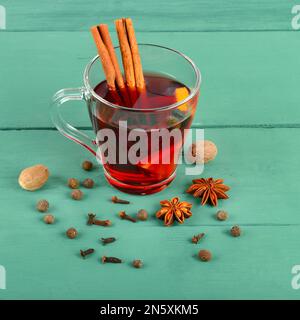 Hot red mulled wine on wooden background with spices, orange slice, anise and cinnamon sticks, close up. Stock Photo