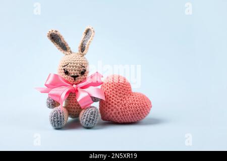 Knitted gray bunny with a crocheted pink heart on a blue background. Happy Valentine's Day, Mother's Day and birthday greeting card. Stock Photo