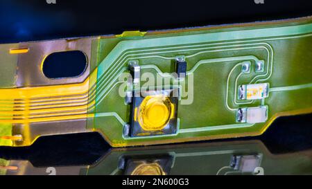 Close-up of electronic flex printed circuit board with reflection on shiny black background. Flat plastic strip with small surface mounted components. Stock Photo
