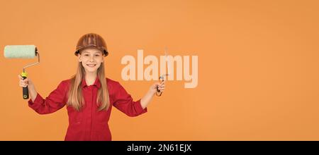 happy teen child in builder hard hat with paint roller and spatula on orange wall Stock Photo