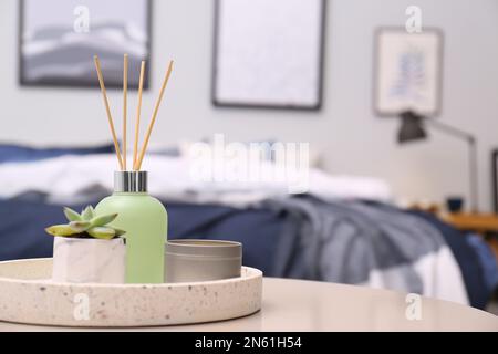 Aromatic reed air freshener, candle and houseplant on table in room. Space for text Stock Photo