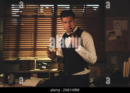 Old fashioned detective with drink and smoking pipe in office Stock Photo