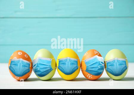 COVID-19 pandemic. Colorful Easter eggs in protective masks on white wooden table Stock Photo