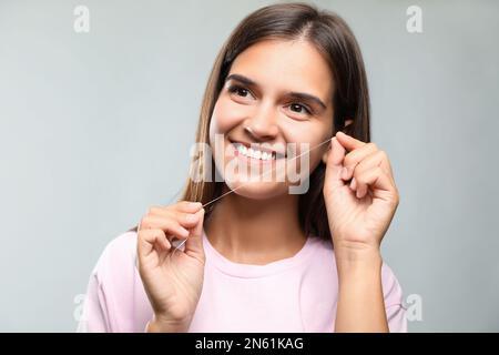 Young woman flossing her teeth on light grey background. Cosmetic dentistry Stock Photo