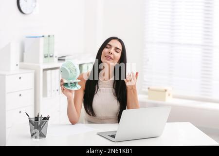 Young woman enjoying air flow from fan at workplace Stock Photo