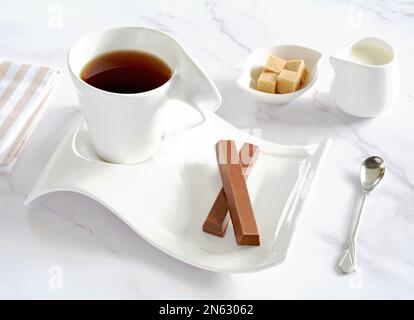 Chocolate wafer biscuits and black tea in white china with milk and sugar on marble background in horizontal format. Stock Photo