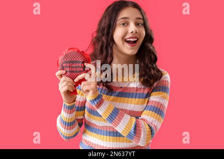 Teenage girl with whoopee cushion on red background. April Fools' Day celebration Stock Photo