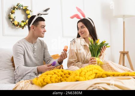 Happy young couple with Easter eggs and tulips in bedroom Stock Photo