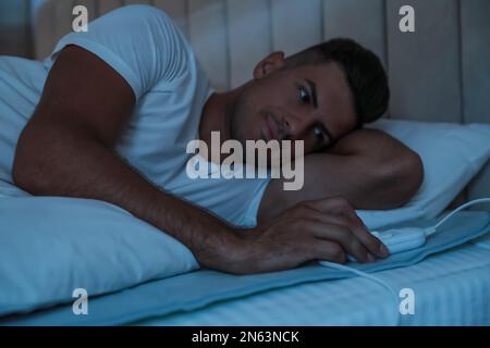 Man switching on electric heating pad in bed at night Stock Photo