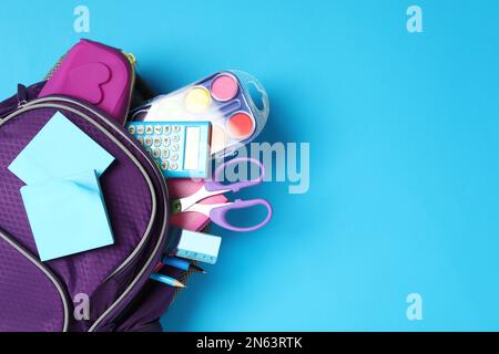 Purple backpack with different stationery on light blue background, top view and space for text. Back to school Stock Photo