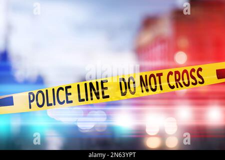 Yellow law enforcement tape isolating crime scene. Blurred view of city, toned in red and blue police car lights Stock Photo