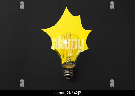 Lamp bulb with yellow paper imitating light on black background, flat lay Stock Photo