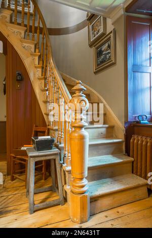 Curved wooden staircase with fancy post and balusters on ground floor inside old circa 1805 cottage style home. Stock Photo