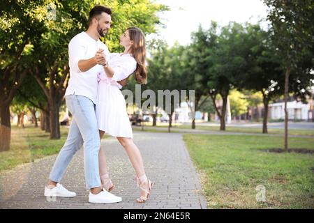 Lovely young couple dancing together in park on sunny day Stock Photo