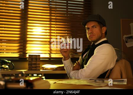 Old fashioned detective with drink at table in office Stock Photo