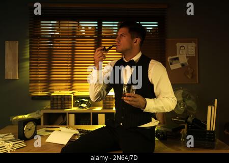 Old fashioned detective with drink and smoking pipe in office Stock Photo