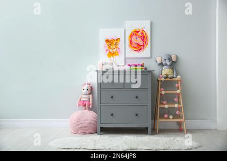 Cute pictures and chest of drawers with toys in baby room interior. Space for text Stock Photo