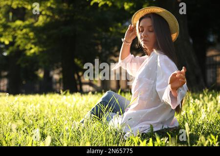 Young woman in straw hat sitting outdoors on sunny day, space for text Stock Photo