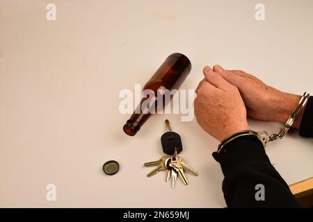 Handcuffed wrists with vehicle keys and alcohol containers symbols of substance use and driving. Stock Photo