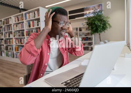 Frustrated student guy in library looking at laptop having tech problems during online learning Stock Photo