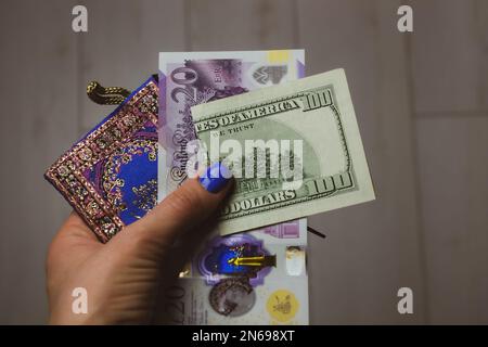 London, UK. May 1, 2022 New bill of 20 British pounds GBP and 100 U.S. dollars USD in a blue woman's purse in hands. Economy, finance, spending, shopp Stock Photo