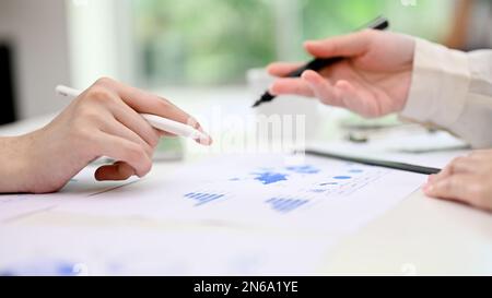 Side view image, Two businesspeople or female financial analysts discussing, analyzing financial data and working on report together in the office. Stock Photo
