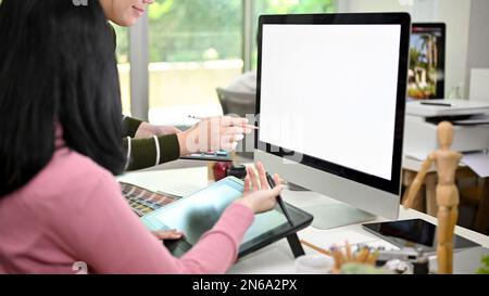 Two creative Asian female graphic designers working together in the studio, discussing and planning their new project. computer white screen mockup Stock Photo