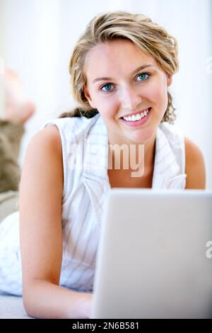 Cute blonde woman relaxing with her laptop while lying on a sofa in her ...
