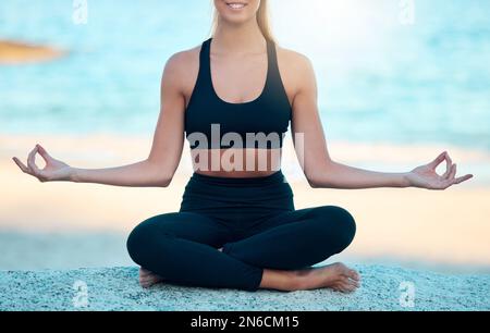 Beautiful woman meditating while practising yoga exercise on the beach. Young zen female athlete working out outside. Finding inner peace, balance and Stock Photo