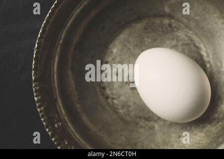 One white fresh organic free range chicken egg in copper bowl on black rustic background. Top view shot. Stock Photo