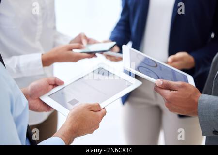 Unknown group of diverse businesspeople using technology in office huddle. Team of colleagues standing together, using bluetooth to sync data and Stock Photo