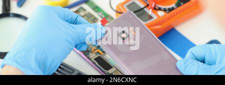 Technician repairs broken smartphone at table in workshop Stock Photo