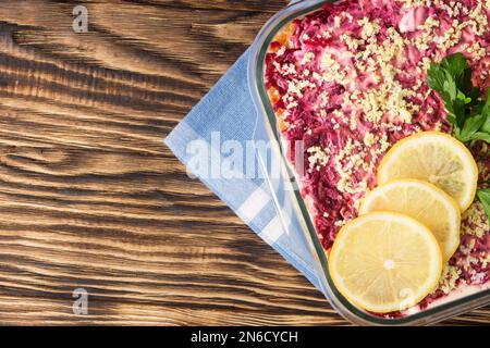 Herring under fur coat. Traditional Russian salad herring under a fur coat, vintage wood background. Layered salad with herring, beets, carrots, onion Stock Photo