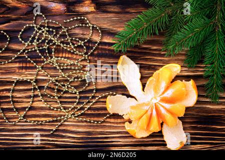 Tangerines close - up on a wooden table near the coniferous branches of spruce. Peeled tangerine near the garland. Christmas background. Flatlay. Top Stock Photo