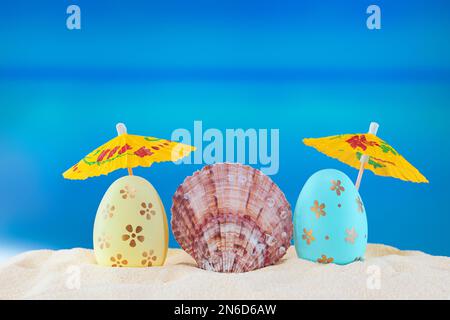 Happy easter. Yellow and blue eggs with conch shell under umbrellas on sandy beach of the sea or ocean. Holiday postcard in hot country. Travel, sprin Stock Photo