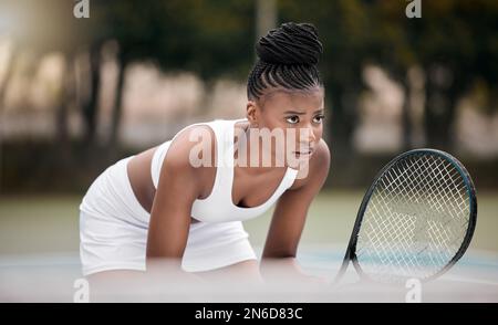 Focused woman waiting during a tennis match. Young african american woman holding her racket during a game of tennis. Professional athlete standing on Stock Photo