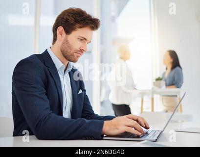 Focused young caucasian businessman typing on a laptop keyboard in an office. Dedicated entrepreneur browsing online while completing deadlines and Stock Photo