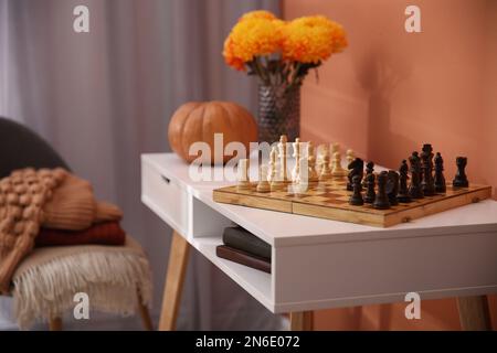 Chess board with pieces on white table in room. Cozy interior inspired by autumn colors Stock Photo