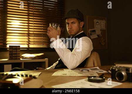 Old fashioned detective with drink at table in office Stock Photo