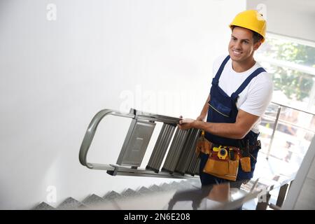 Professional builder carrying metal ladder up stairs Stock Photo