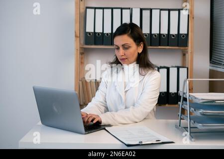 Female doctor working with laptop in clinic at her workplace. Serious physician at work. Perfect medical service and medicine concept. Stock Photo